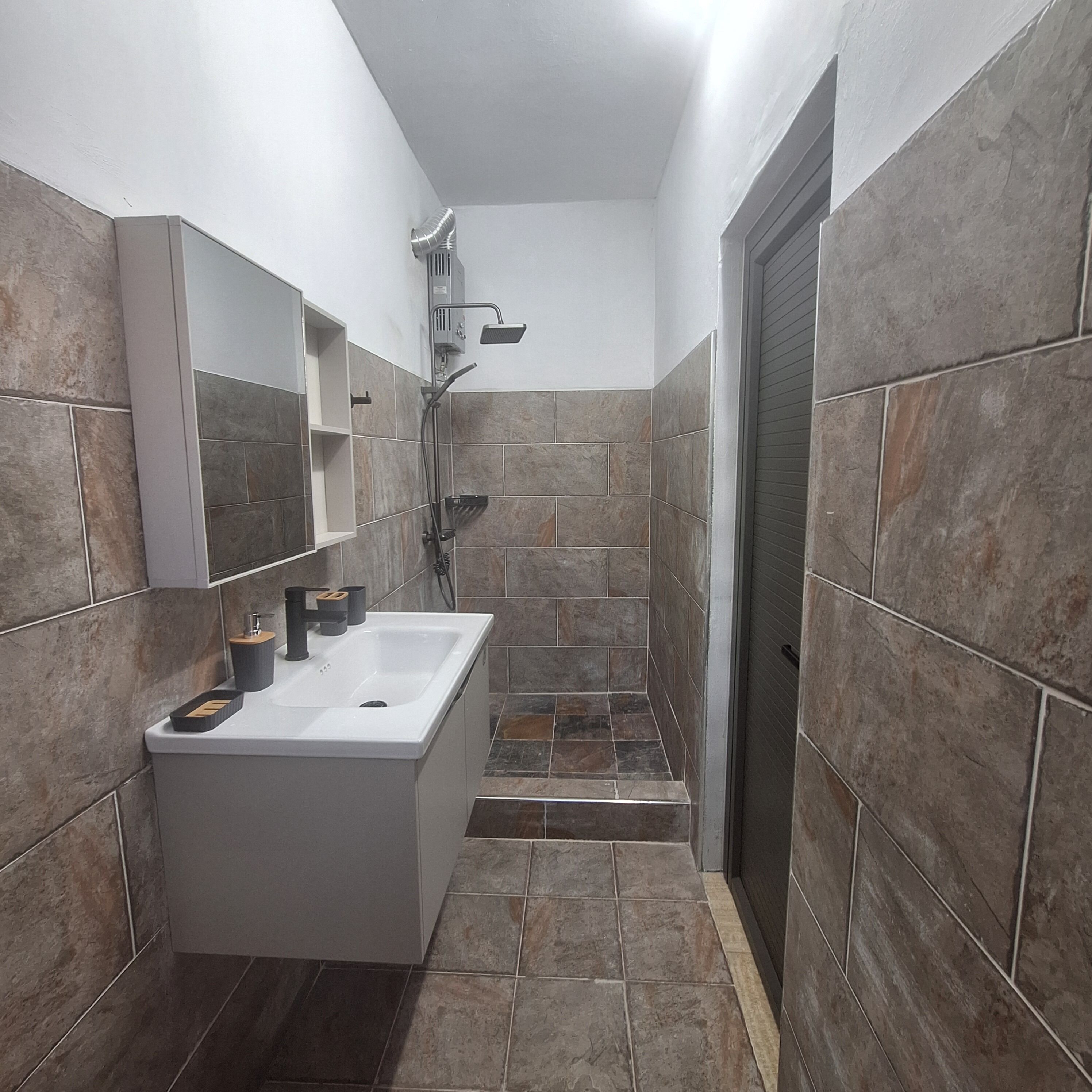 Een badkamer met een witte wastafel, een spiegel en een douchehoek.