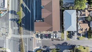 Vista aérea de um estacionamento com carros, uma placa de pare e um edifício com um telhado peculiar.
