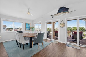A dining area with a wooden table and chairs, a ceiling fan, and a large fish mounted on the wall. - Lovely 4-bedroom condo in Dewey Beach perched above all the action! (Dewey Beach)