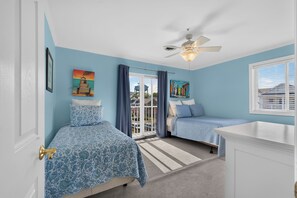 A bedroom with two beds, a ceiling fan, and a view through a glass door. - Lovely 4-bedroom condo in Dewey Beach perched above all the action! (Dewey Beach)