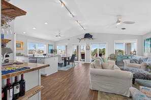 A spacious living area with a dining table, a kitchen with a wooden countertop, and a large window offering a view of the outside. - Lovely 4-bedroom condo in Dewey Beach perched above all the action! (Dewey Beach)