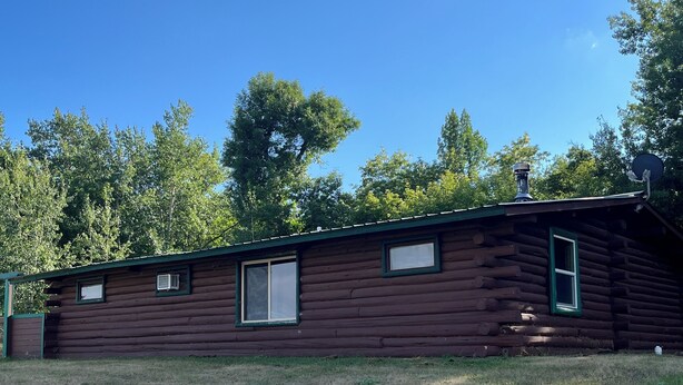 Una cabaña de troncos con chimenea, antena parabólica y una ventana pequeña.