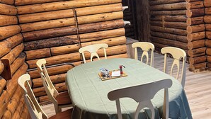 Interior de una cabaña de madera con una mesa de comedor lista para cuatro personas, rodeada de sillas blancas.