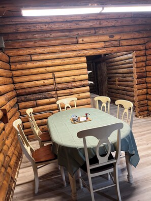 En stuga med träpanel på insidan, där ett matbord är dukat för fyra personer och omgivet av vita stolar.