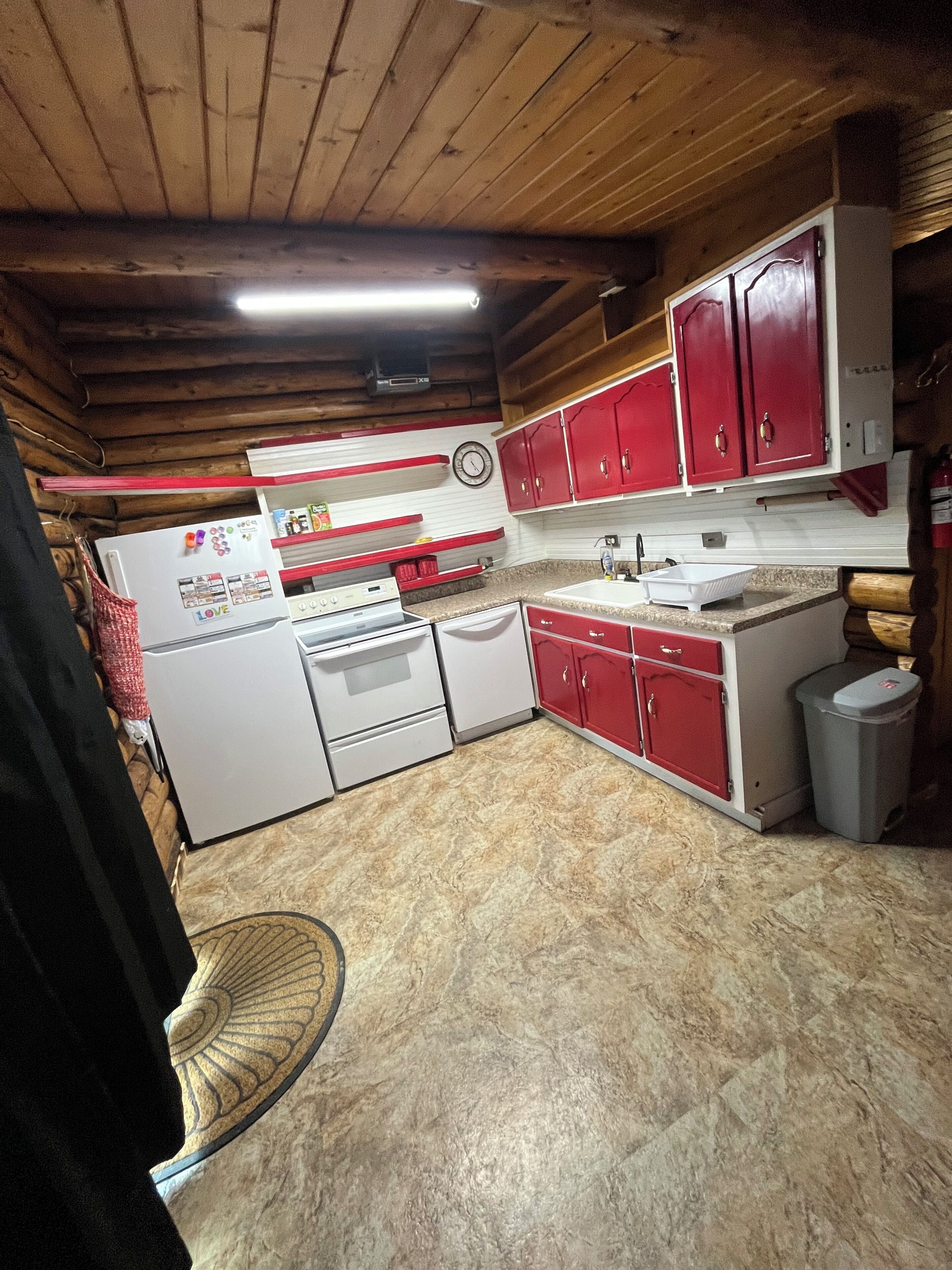 A kitchen with wooden ceiling beams, a white refrigerator, red cabinets, and a white sink.