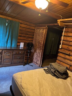 Una habitación de cabaña de madera con una cama, cómoda, ventilador y ventilador de techo.