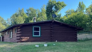 Una cabaña de troncos con chimenea, antena parabólica y un ventanal pequeño.