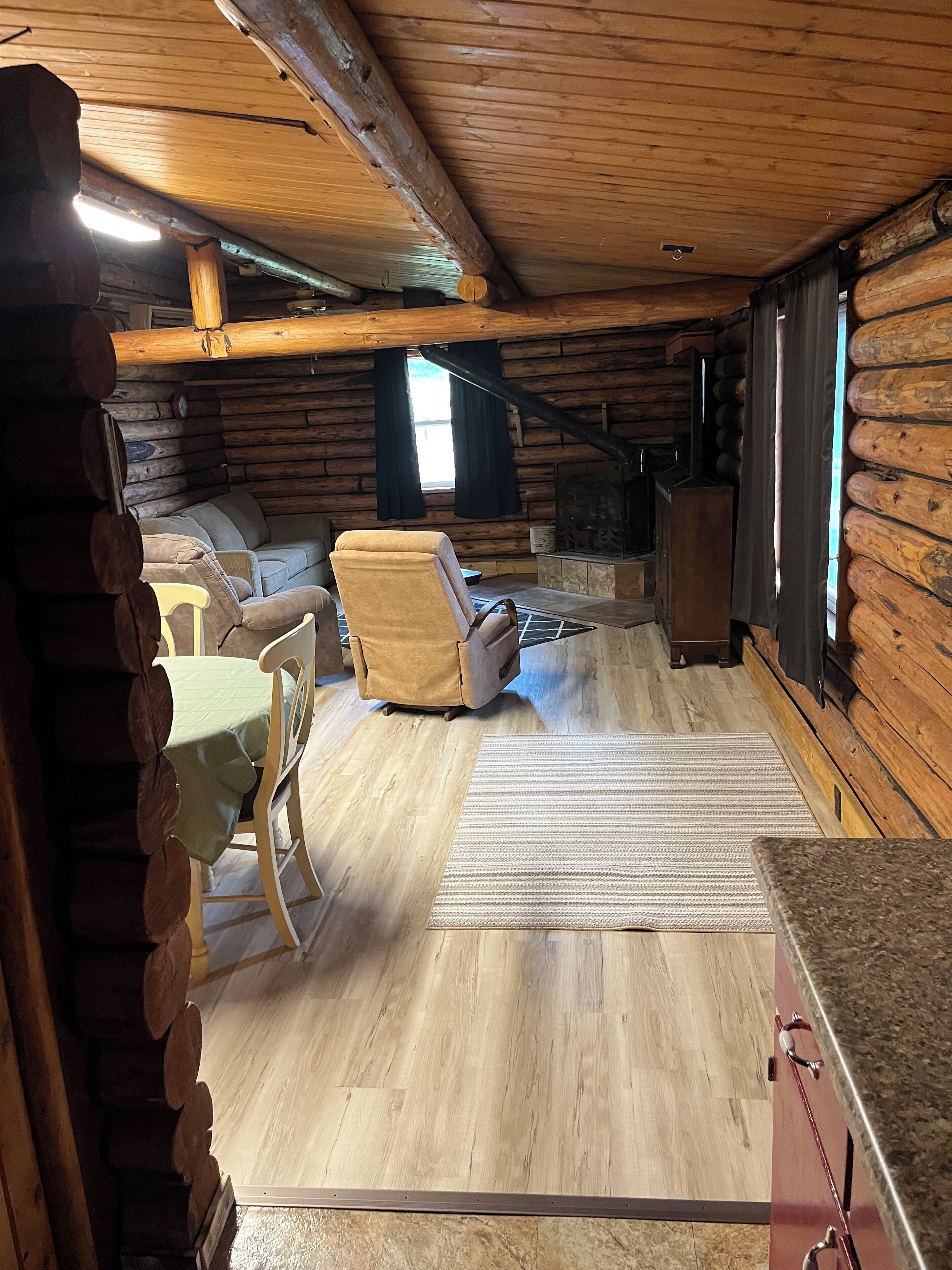 L’intérieur d’une cabane en rondins, avec un canapé, des fauteuils, une cheminée et une table à manger.