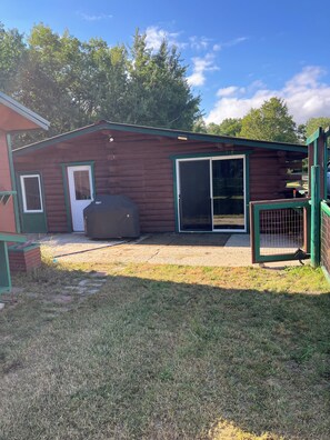 A wooden cabin with a sliding glass door, a small porch, and a fenced area.