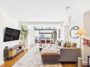 Ein modernes Wohnzimmer mit Flachbildfernseher, einer Couch, einem Couchtisch und einem Essbereich mit Stühlen und Tisch.