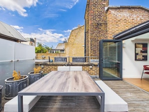 Eine Dachterrasse mit einem Holztisch und -stühlen, einer Backsteinmauer und einer Glastür, die zu einem Innenbereich führt.