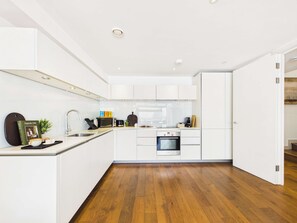 Eine moderne Küche mit weißen Schränken, Holzboden und eingebautem Backofen.