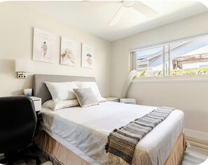 Un dormitorio con cama, escritorio, silla, mesita de noche y ventana con vistas.