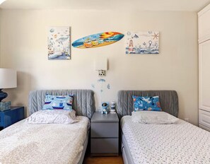 A bedroom with two beds, each with a pillow featuring nautical designs. There is a nightstand between the beds with a lamp and a small decorative item. - San Diego Family Getaway /Private Fire Pit (San Diego)