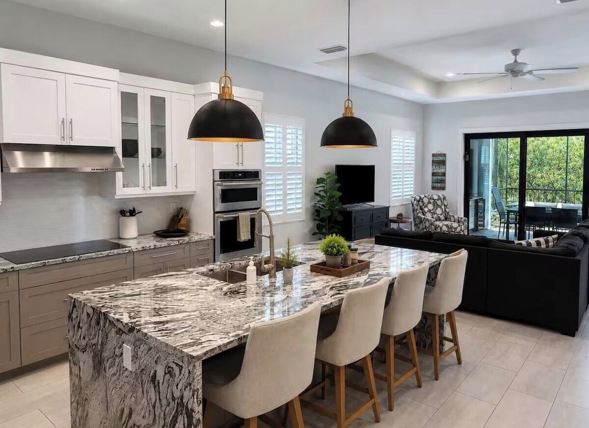 A modern kitchen with a marble island, pendant lighting, and a dining area with a black sofa.