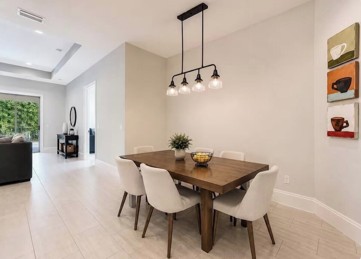 A dining area with a wooden table, white chairs, and a hanging light fixture.