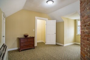 A room with a patterned carpet, a wooden dresser, a white door, and a brick wall. - 315 Cozy 2BR – free parking Medium & Long term (Indianapolis)