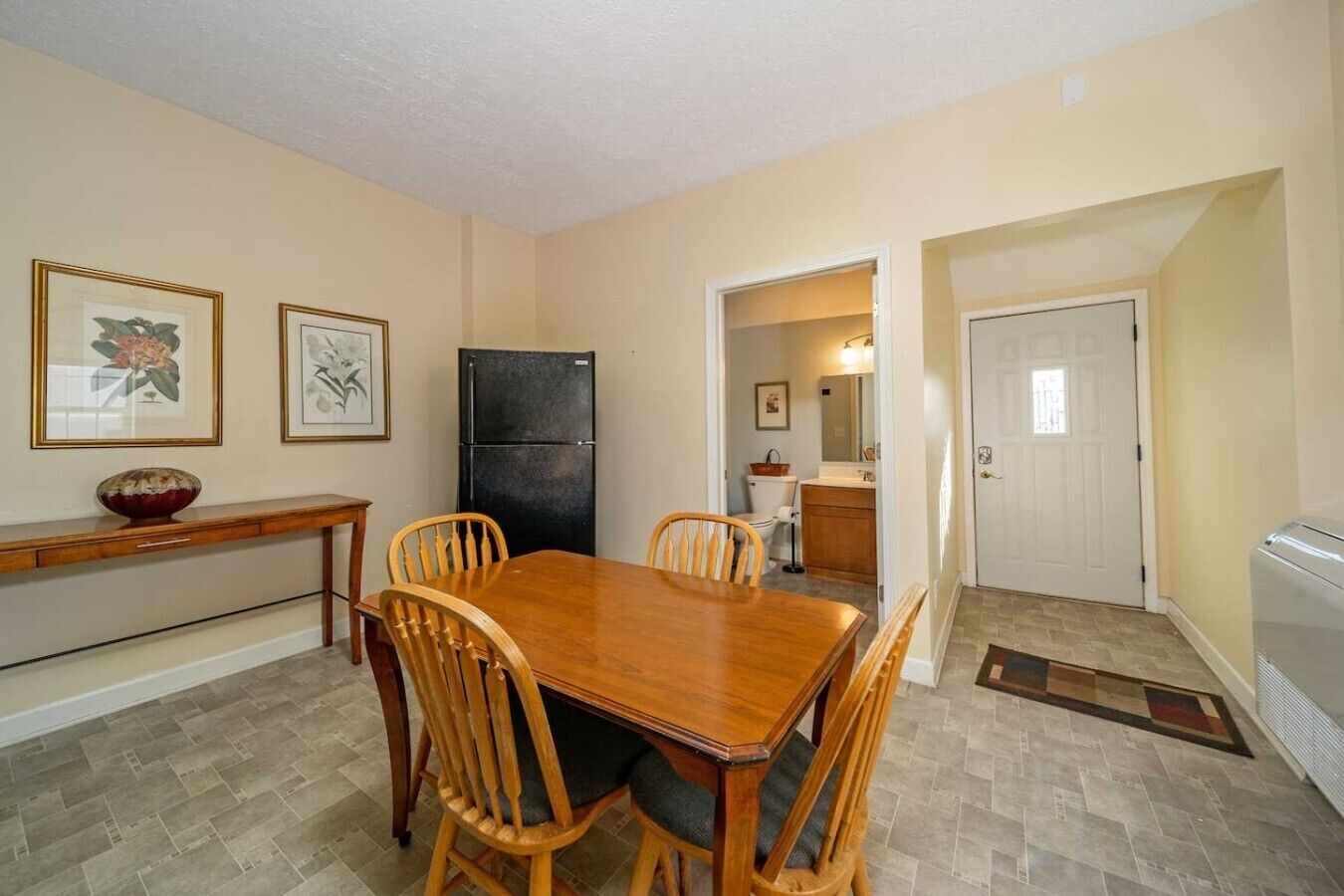 A dining area with a wooden table and chairs, a black refrigerator, and framed artwork on the wall.