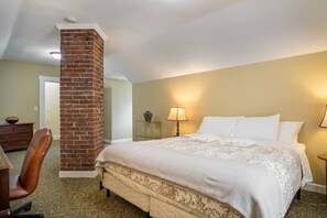 A hotel room with a brick pillar, a bed with white linens, a desk with a lamp, and a chair. - 315 Cozy 2BR – free parking Medium & Long term (Indianapolis)