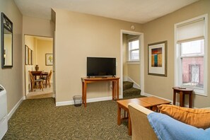 A living room with a television, a dining area with chairs, a staircase, and a window with blinds. - 315 Cozy 2BR – free parking Medium & Long term (Indianapolis)