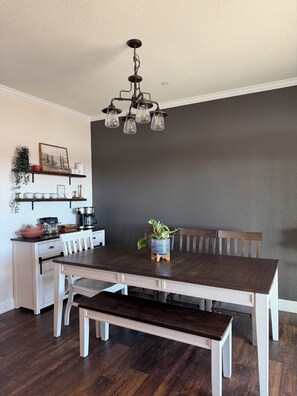 A dining area with a dark wooden table, white chairs, a bench, and a hanging light fixture. - Spacious 4 Bedroom home on an 80 acre horse ranch- 15 minutes from Wine Country (Hemet)