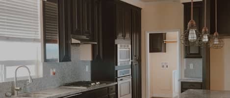 A modern kitchen with dark cabinetry, granite countertops, stainless steel appliances, and pendant lighting.