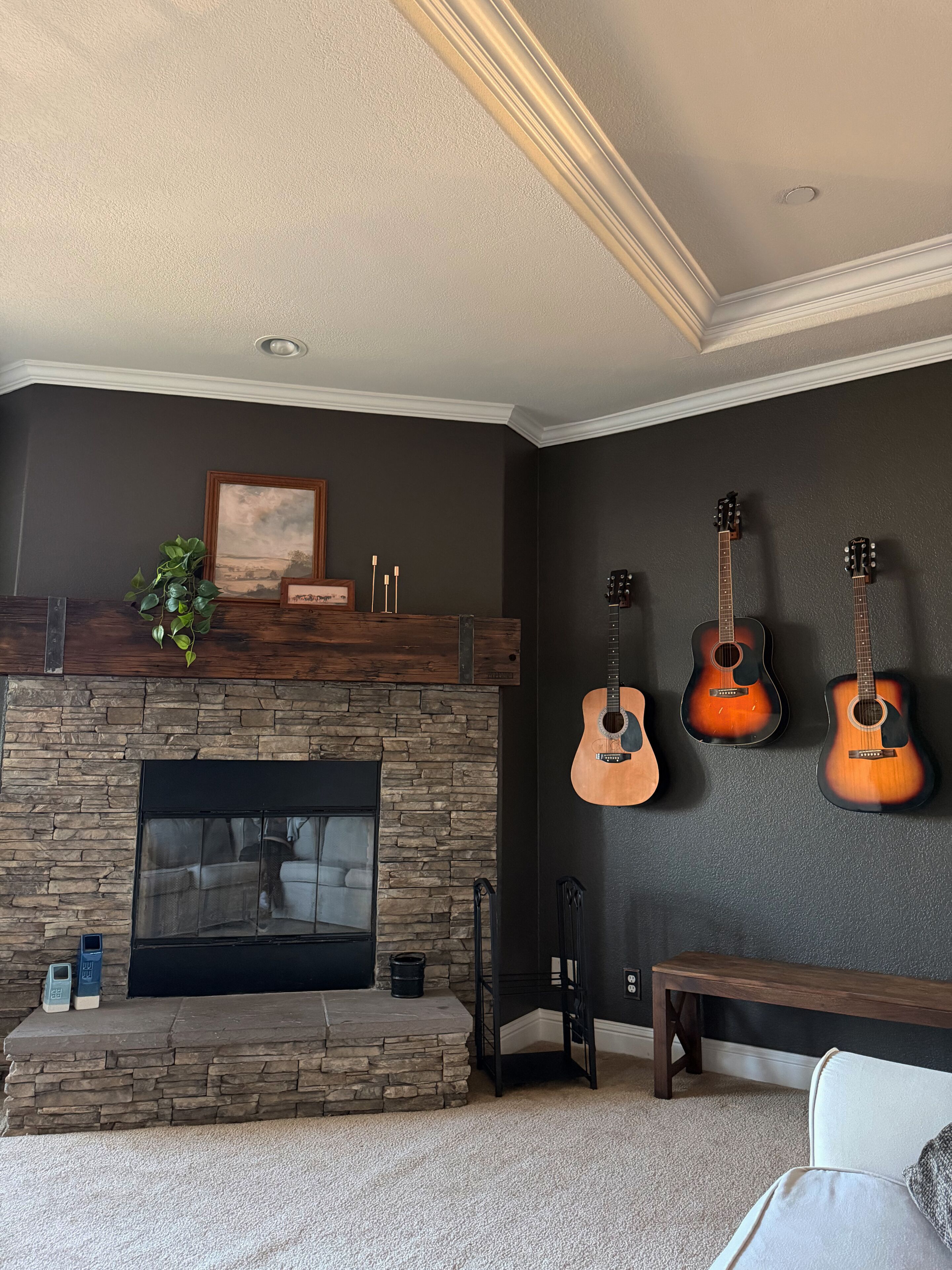 A living room with a stone fireplace, a couch, and three guitars on the wall.