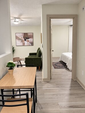 Ein modernes Wohnzimmer mit Essbereich, einem grünen Sofa, einem Bett mit weißer Bettwäsche und einem Deckenventilator.