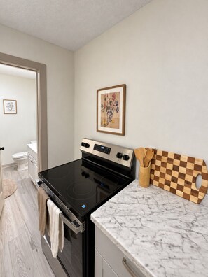 A modern kitchen with a black stove, a marble countertop, and a checkered cutting board. - 204 Charming Studio, DT Indy, Medium & Long Stays! (Indianapolis)