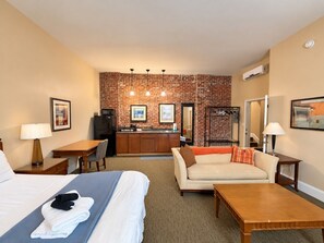 A hotel room with a bed, a sofa, a desk, a kitchenette, and a brick wall. - 203 Studio Near Downtown Indy - Med/Long term (Indianapolis)