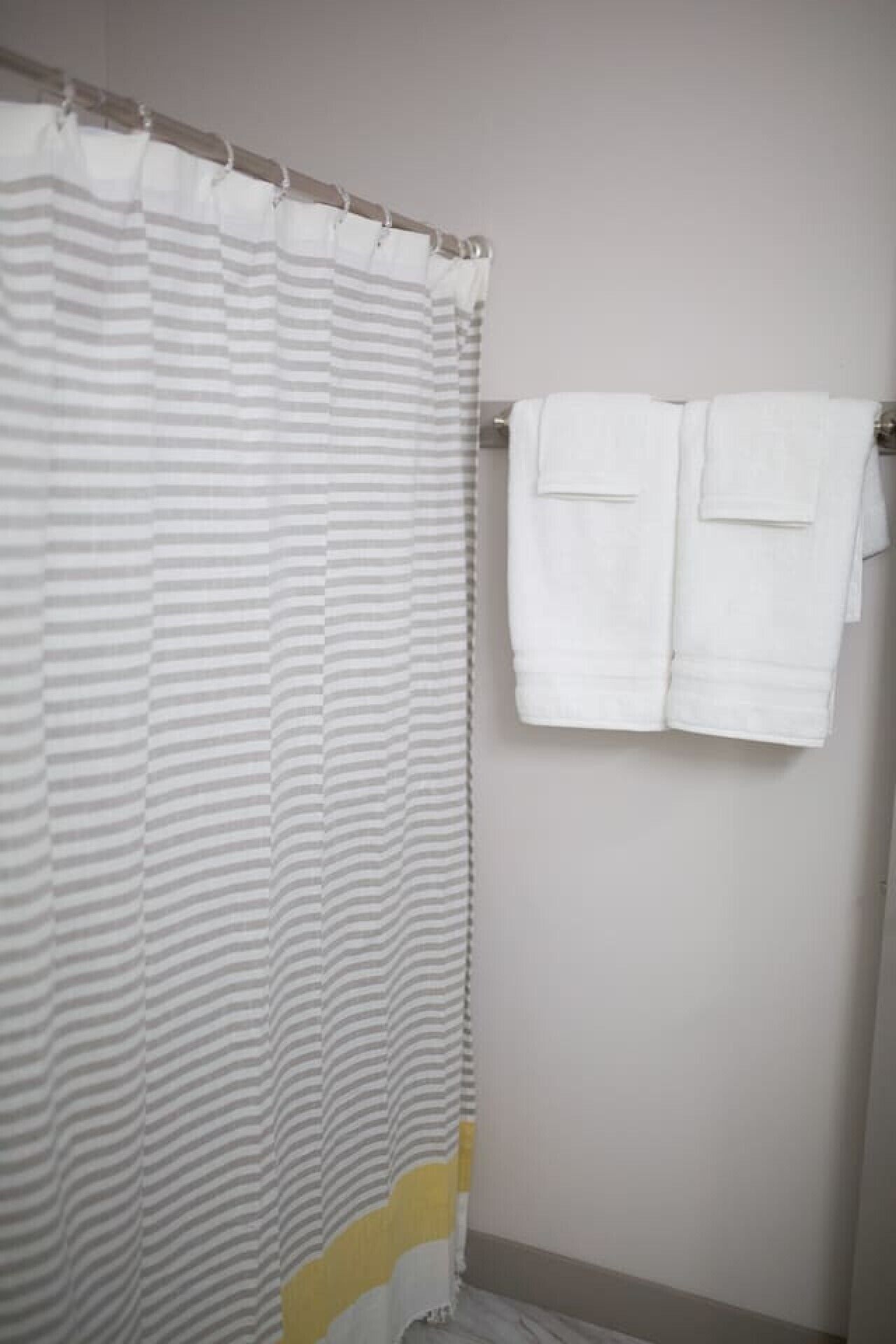 A bathroom with a striped shower curtain, two white towels hanging on a rack, and a plain wall.
