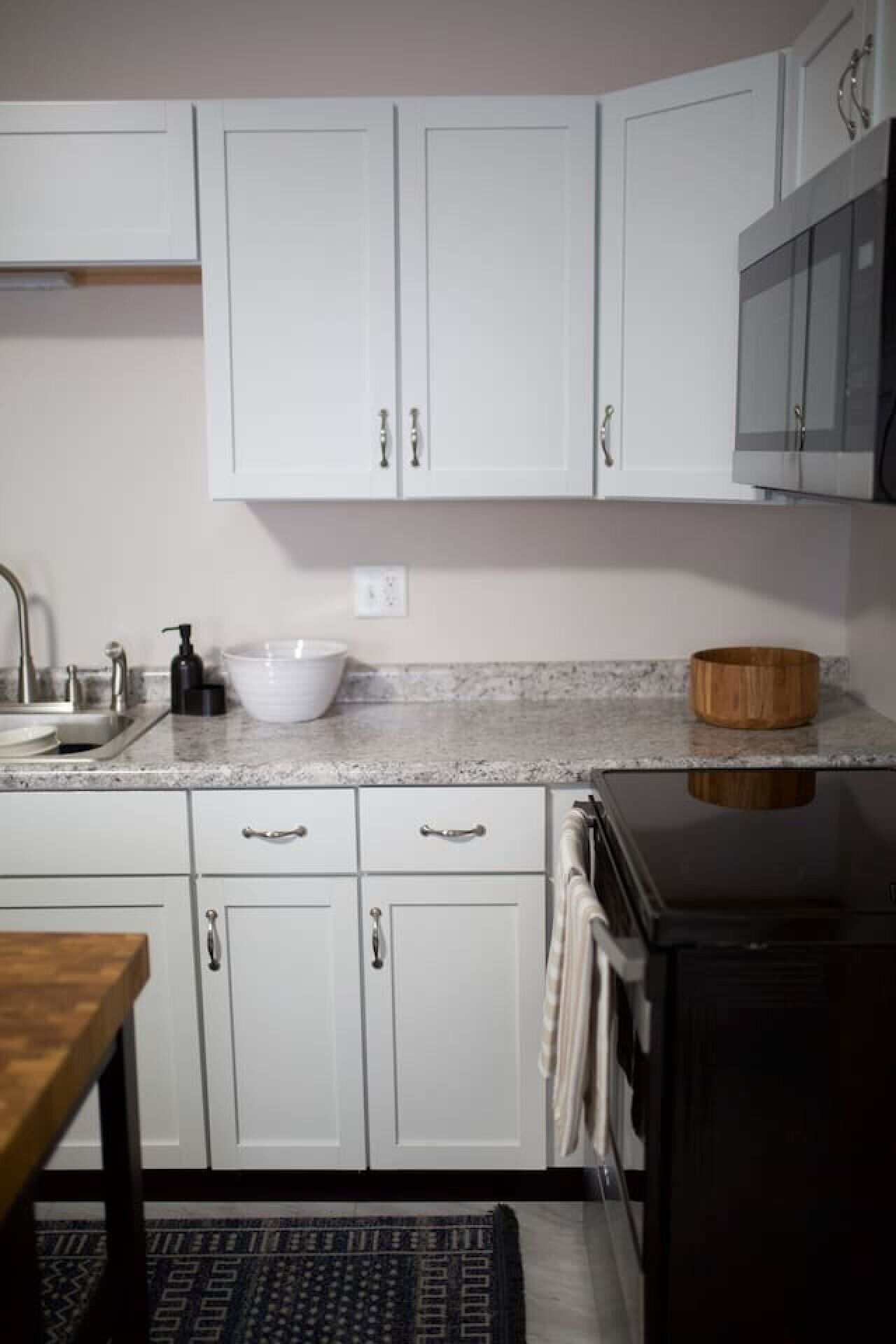 A kitchen with white cabinets, a granite countertop, a sink, a wooden bowl, and a black refrigerator.