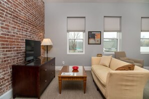 Ein Wohnzimmer mit Backsteinwand, einem Fernseher, einer Couch, einem Couchtisch und einer Lampe.