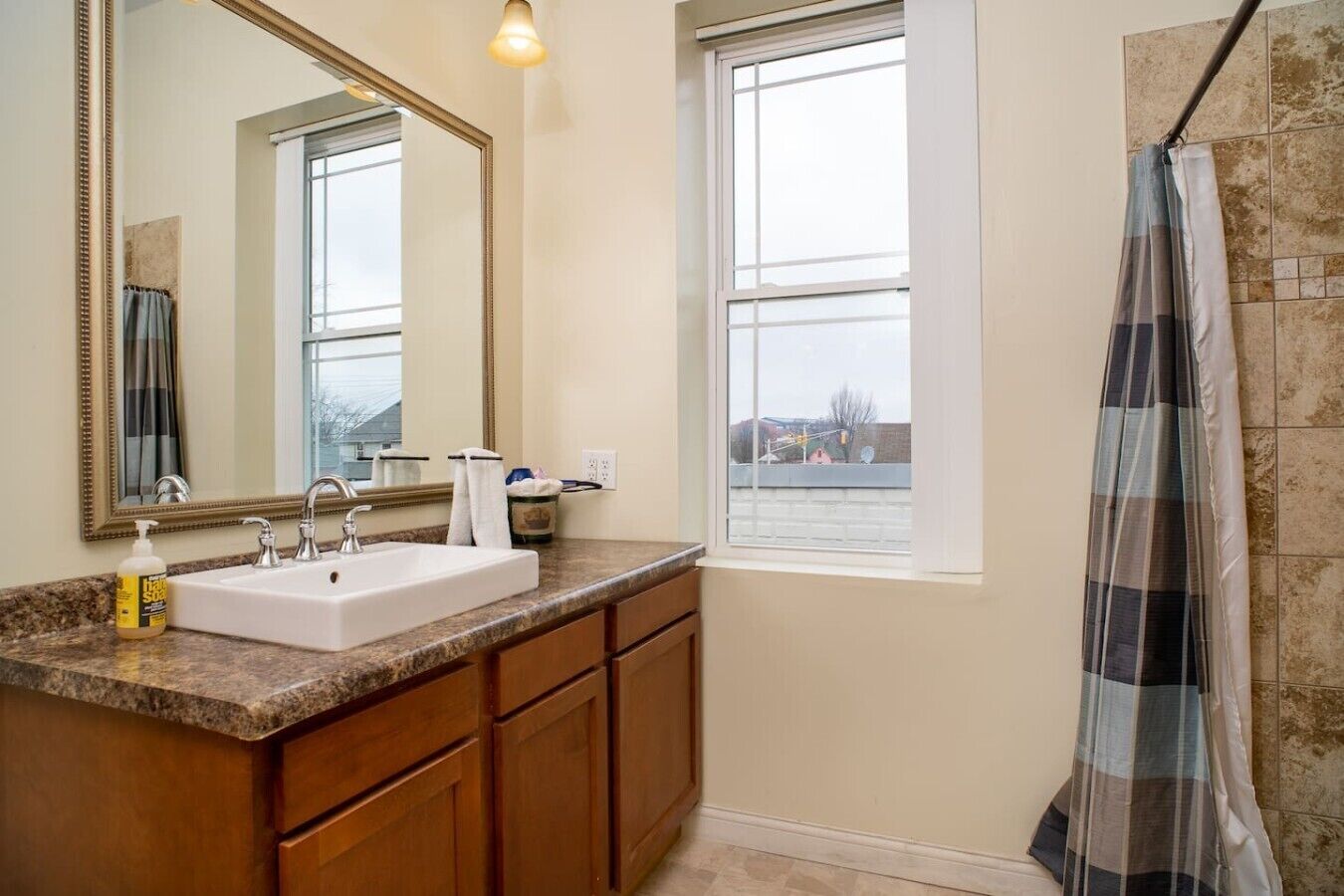 A bathroom with a white sink, wooden cabinets, a large mirror, and a window with a view.