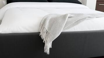 A bed with a dark headboard, white bedding, and a white fringed throw blanket.