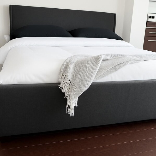A bed with a dark headboard, white bedding, and a white fringed throw blanket.