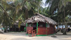 A thatched-roof hut with a wooden porch, surrounded by palm trees on a sandy beach. - Beachfront Cabin on the San Blas Islands: Aroma (Guna Yala)