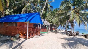A wooden structure with a blue roof, surrounded by palm trees and a sandy beach. - Beachfront Cabin on the San Blas Islands: Aroma (Guna Yala)