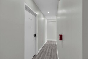 Een gang met een witte deur met de tekst 'SUITE 204', een rode noodtelefoon en een lichtgekleurde houten vloer.