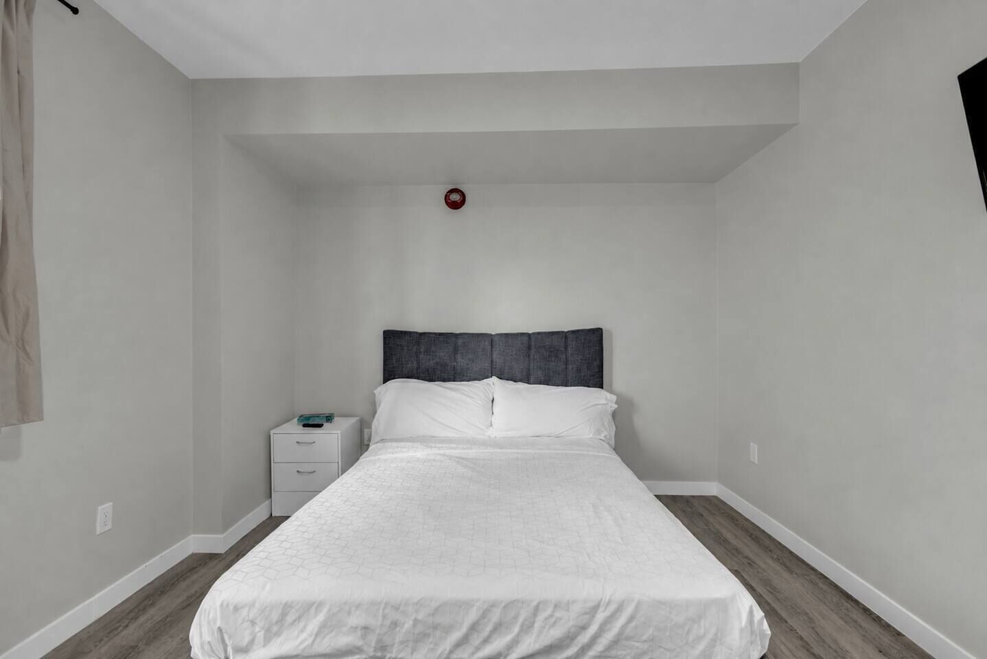 A bedroom with a bed, nightstand, and a red emergency light.