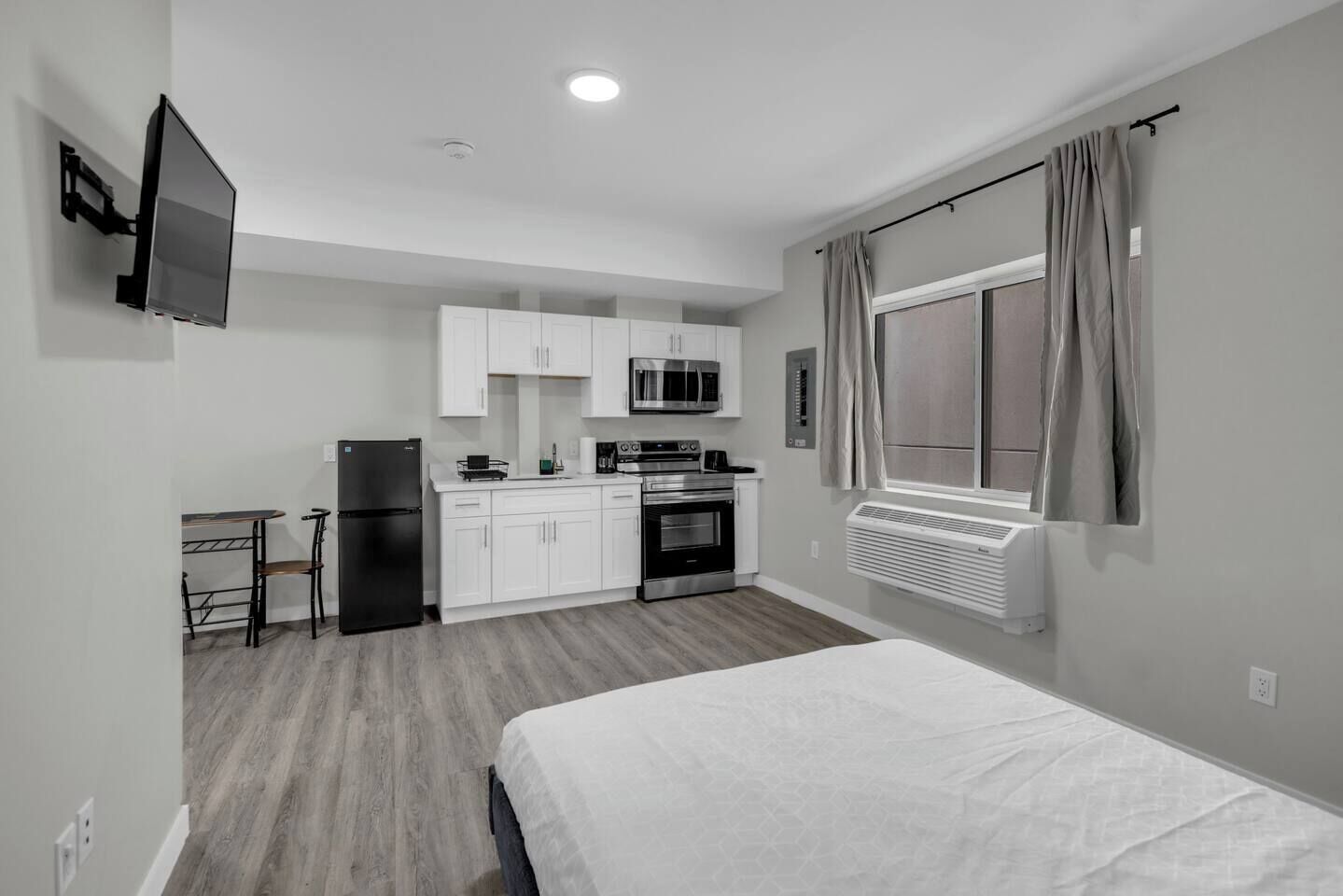 Ein kleines Hotelzimmer mit Bett, Küchenzeile und einem Vorhangfenster.