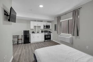 A compact hotel room with a bed, kitchenette, and a window with curtains. - The Platinum Suite • Studio • DT Oshawa (Oshawa)