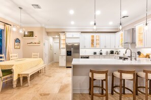 Une cuisine moderne avec des meubles blancs, un îlot central doté de tabourets, et un coin repas avec un banc et une table.