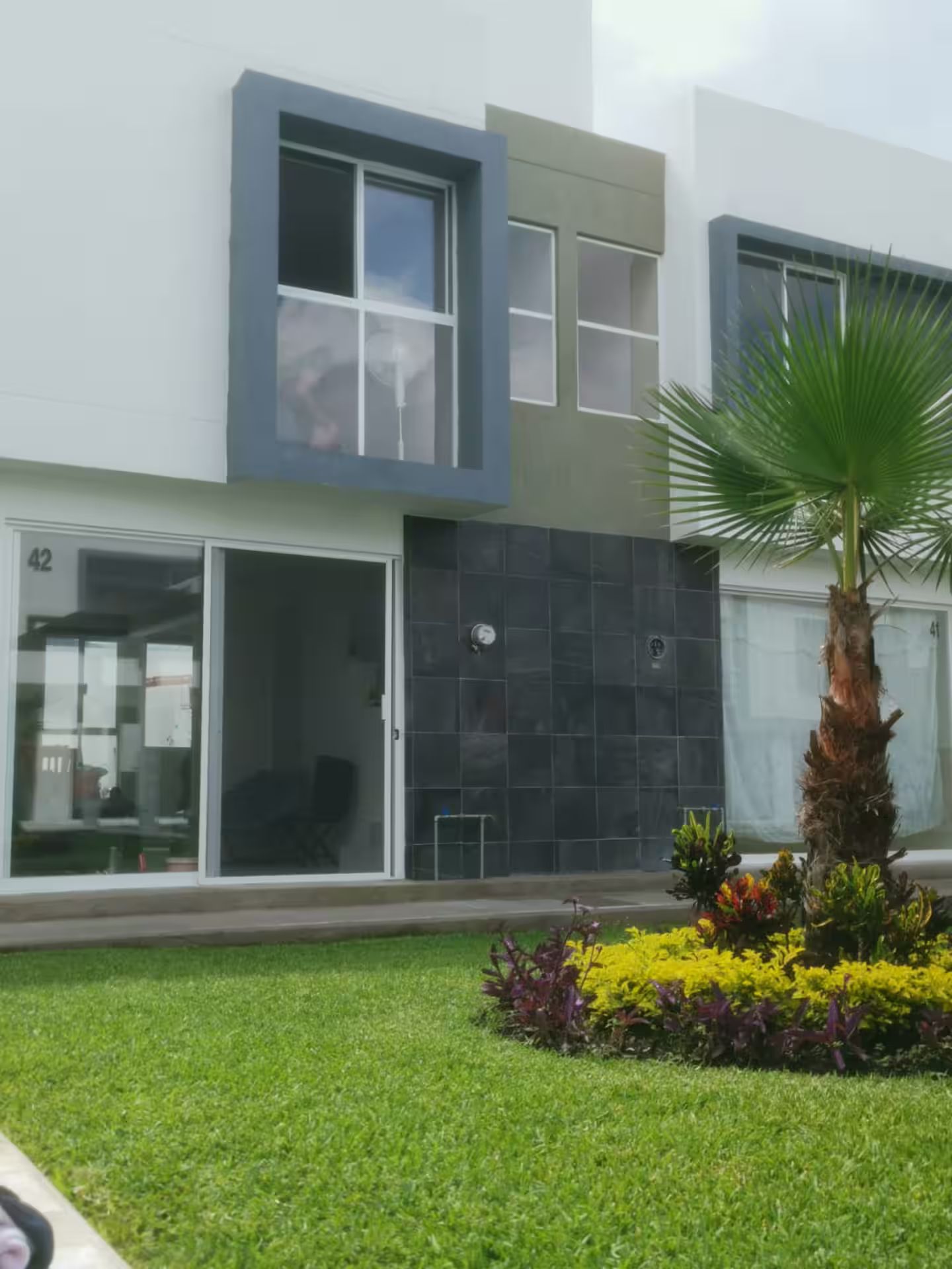 Een modern gebouw met een plat dak, grote ramen en een verzorgd gazon met kleurrijke bloemen.