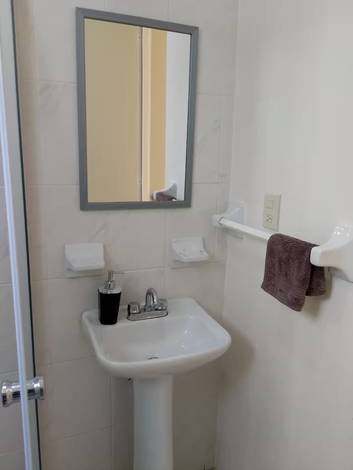 Un baño con lavamanos blanco, un espejo y un perchero para toallas.