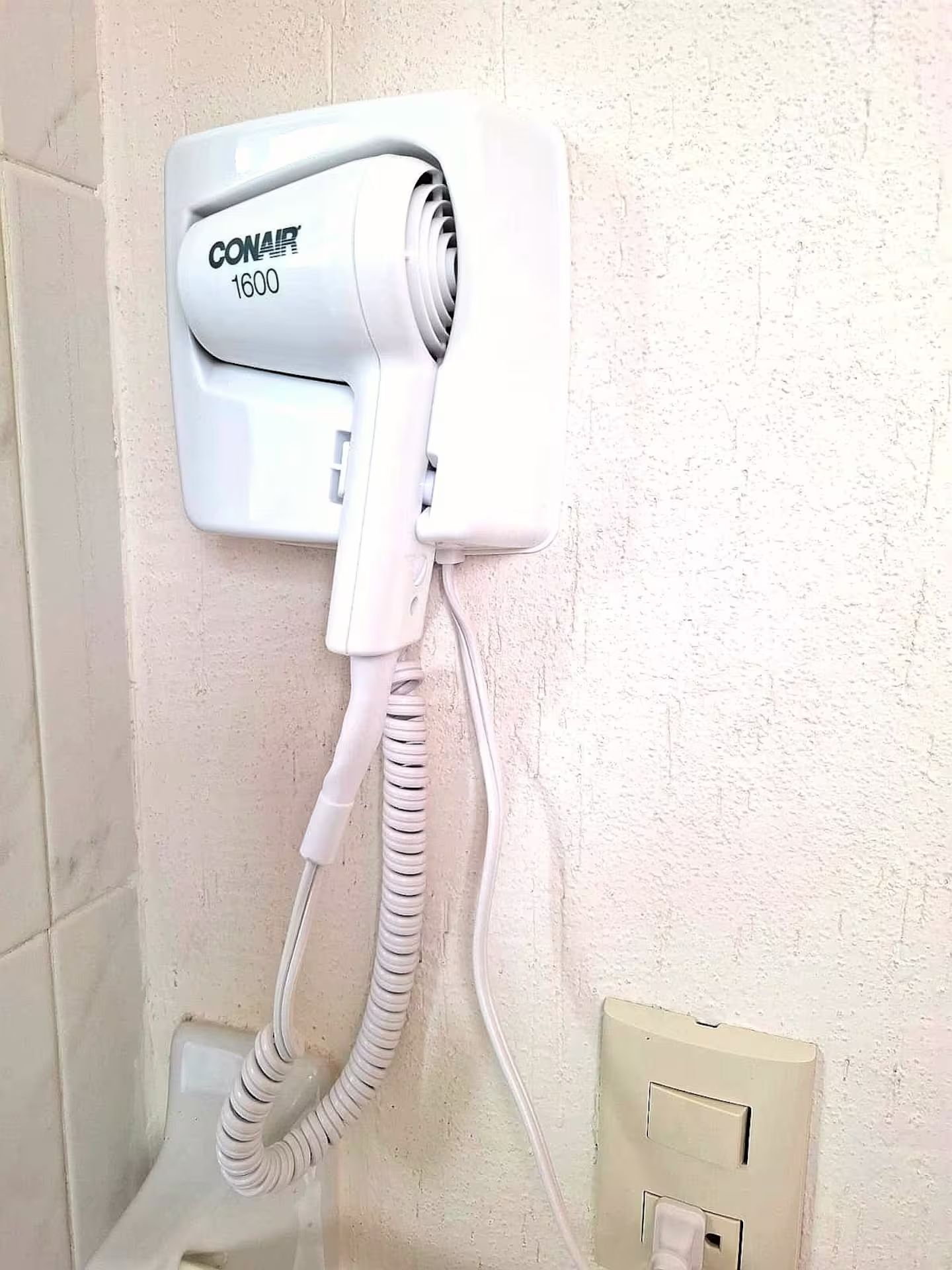Secador de cabelo fixado na parede com cabo enrolado.