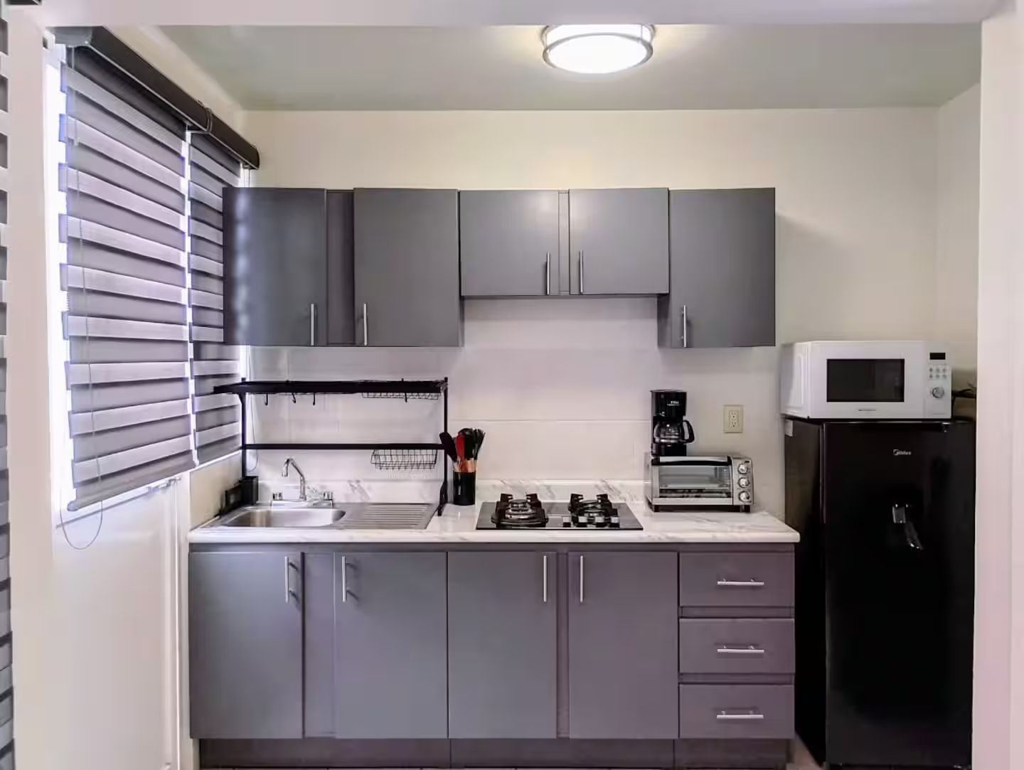 A compact kitchen with grey cabinets, a microwave, a toaster, and a coffee maker.