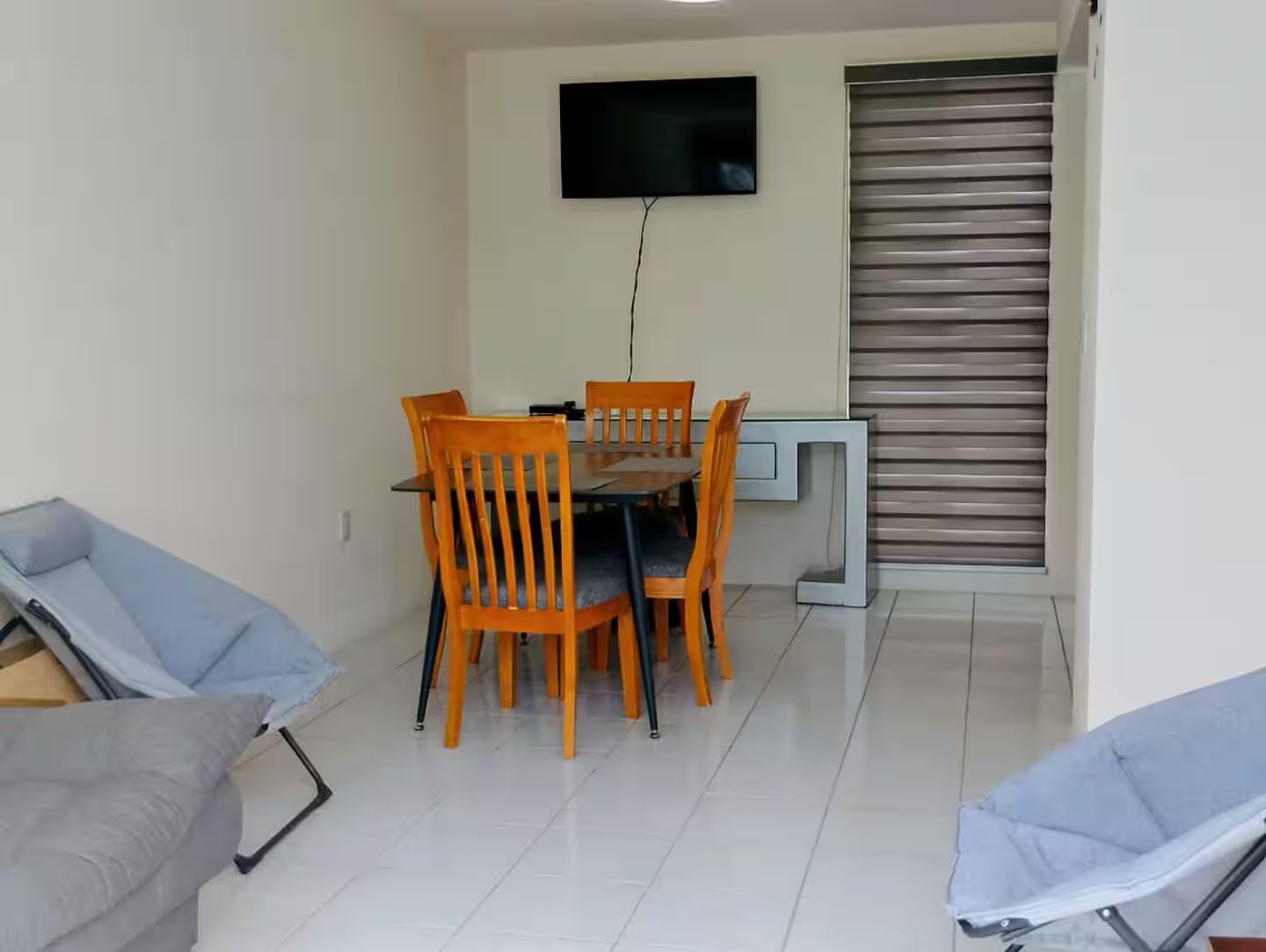 A dining area with a table and chairs, a television mounted on the wall, and a sliding door.