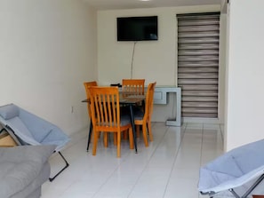 A dining area with a table and chairs, a television mounted on the wall, and a sliding door.
