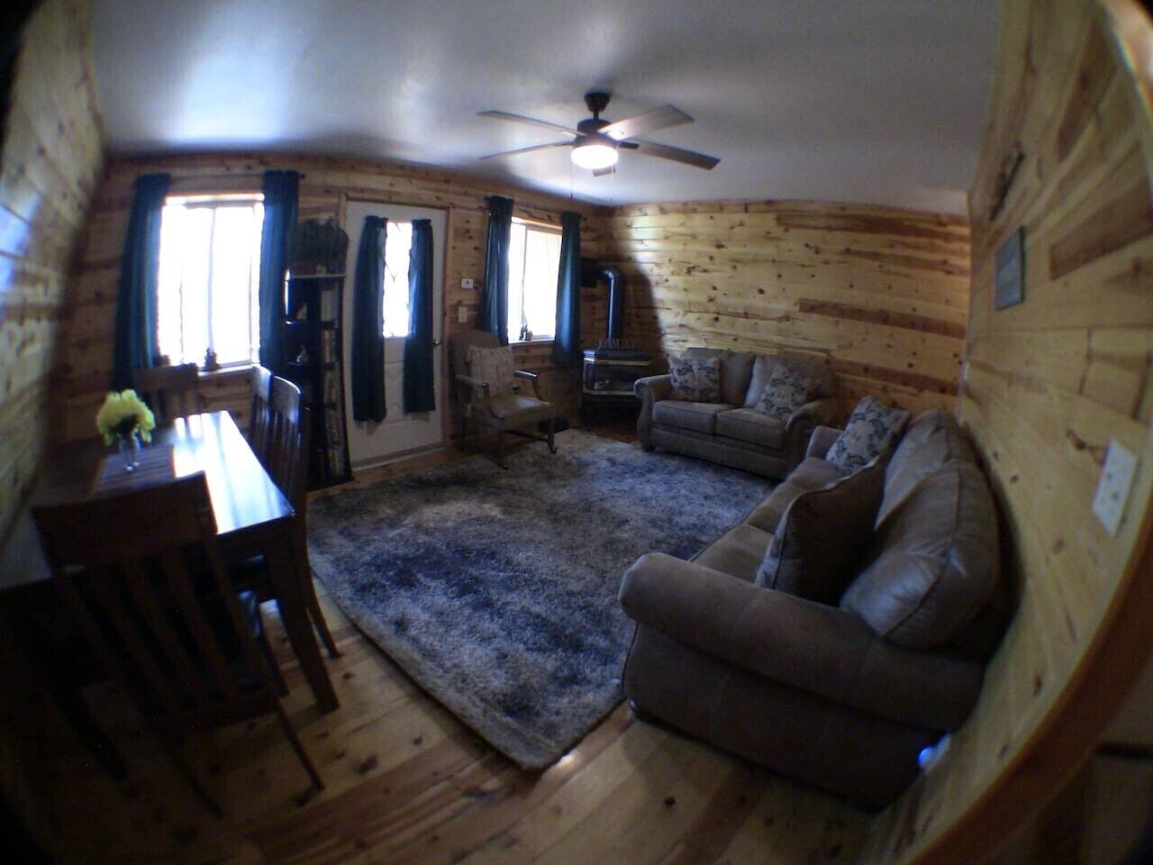 A room with a ceiling fan, wooden walls, a sofa, a coffee table, and a rug.